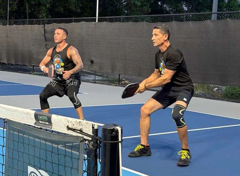 Two players in a doubles rally on the outdoor courts at Dink Club in Miami